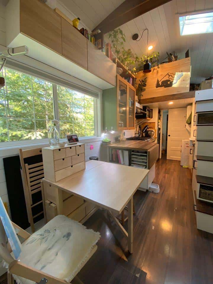 Compact tiny house kitchen with large window and modern appliances.