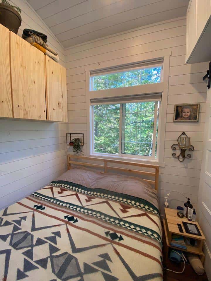Cozy tiny house bedroom with natural light and forest views in a Kootenay, BC community.
