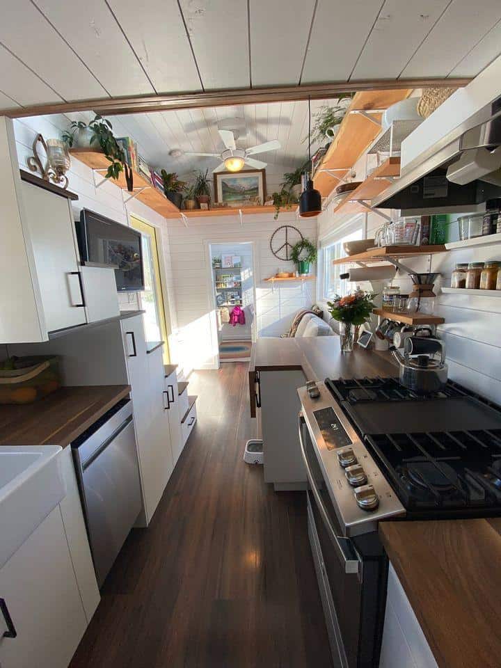 Compact tiny house kitchen with modern appliances and open shelving.