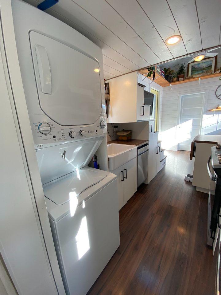 Compact tiny house kitchen featuring stacked washer and dryer unit.