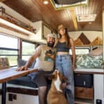 Bus conversion interior with a couple and dog, showcasing small space living and freedom.