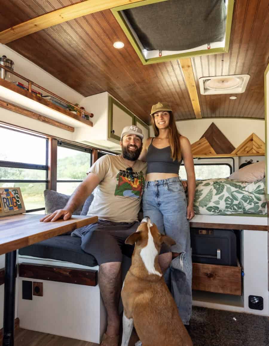 Bus conversion interior with a couple and dog, showcasing small space living and freedom.