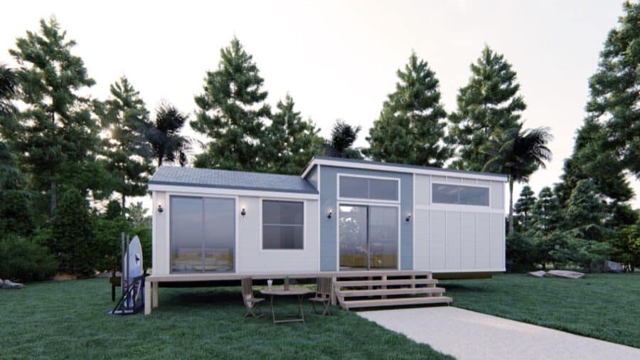 Modern tiny house on wheels with large windows and outdoor deck, set in lush green surroundings.
