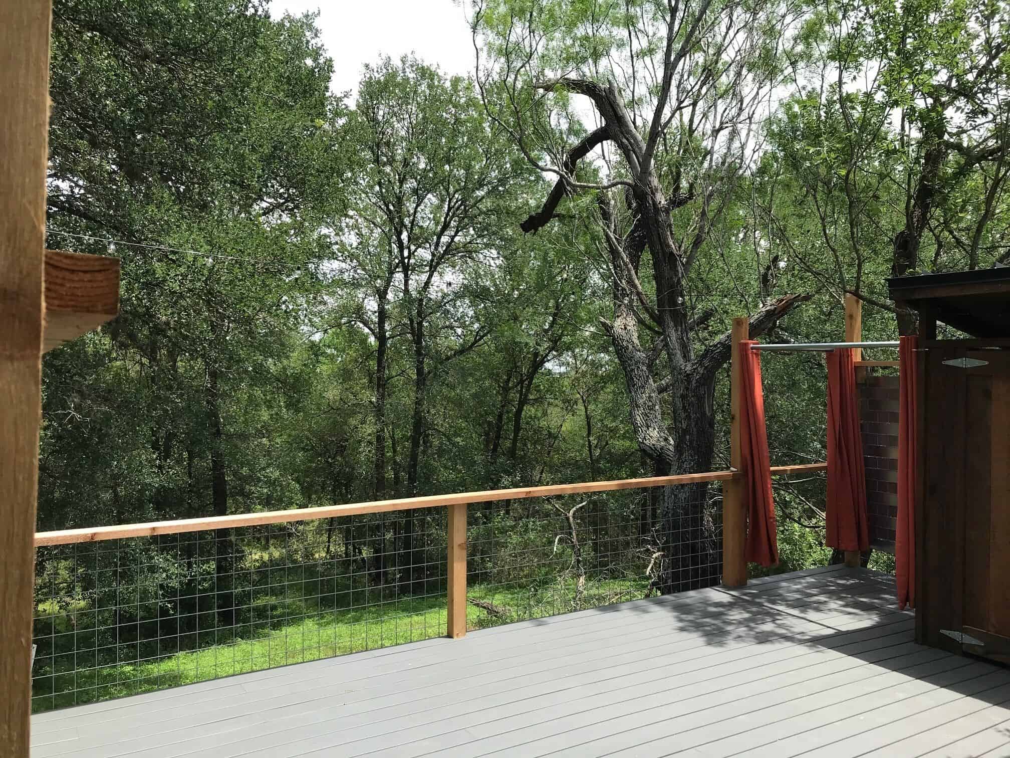 Deck with wire railing overlooking wooded grounds and outdoor shower at Spencer Ranch