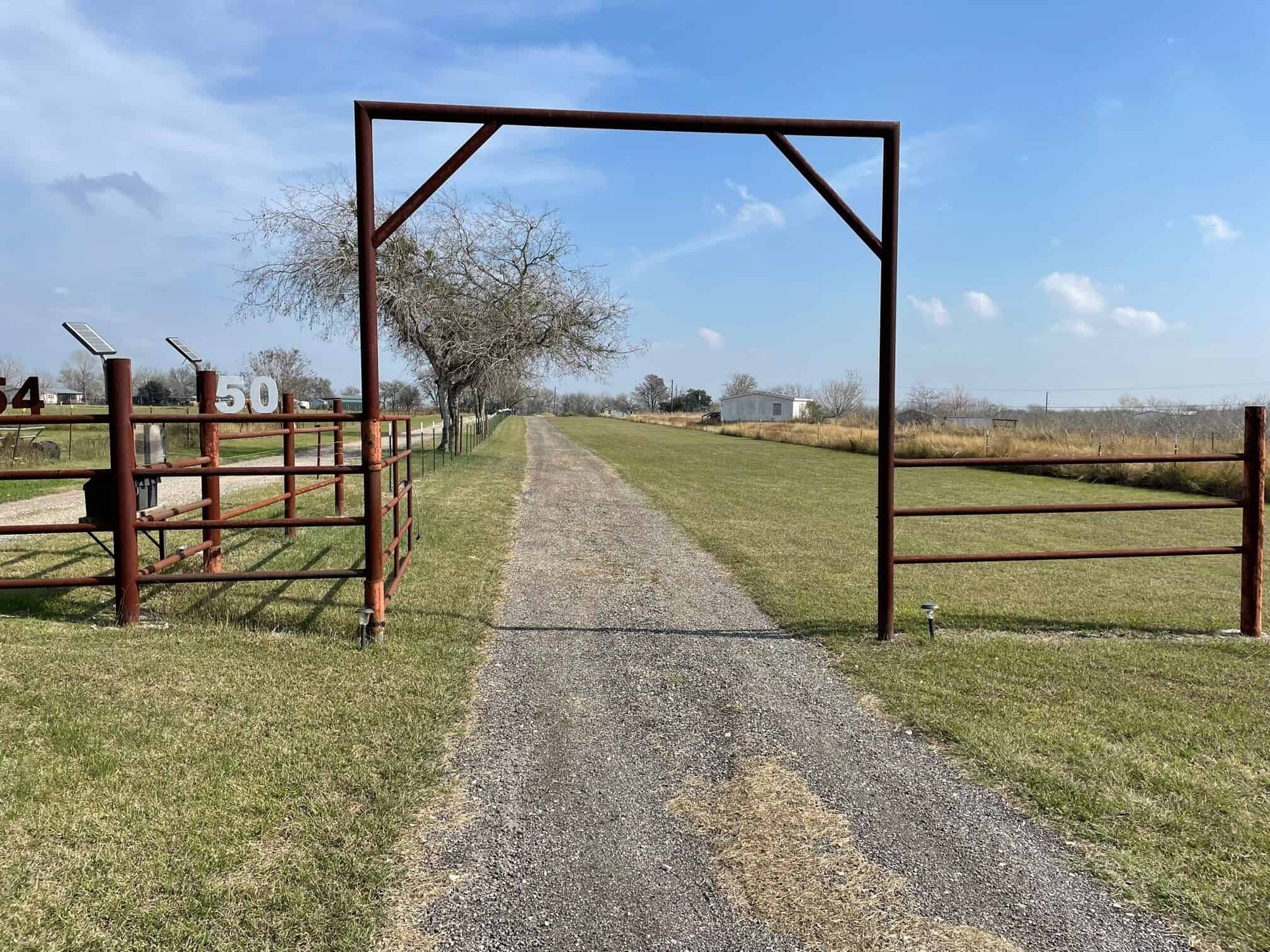 Ranch gate entrance and gravel driveway leading to The Cabin at Spencer Ranch