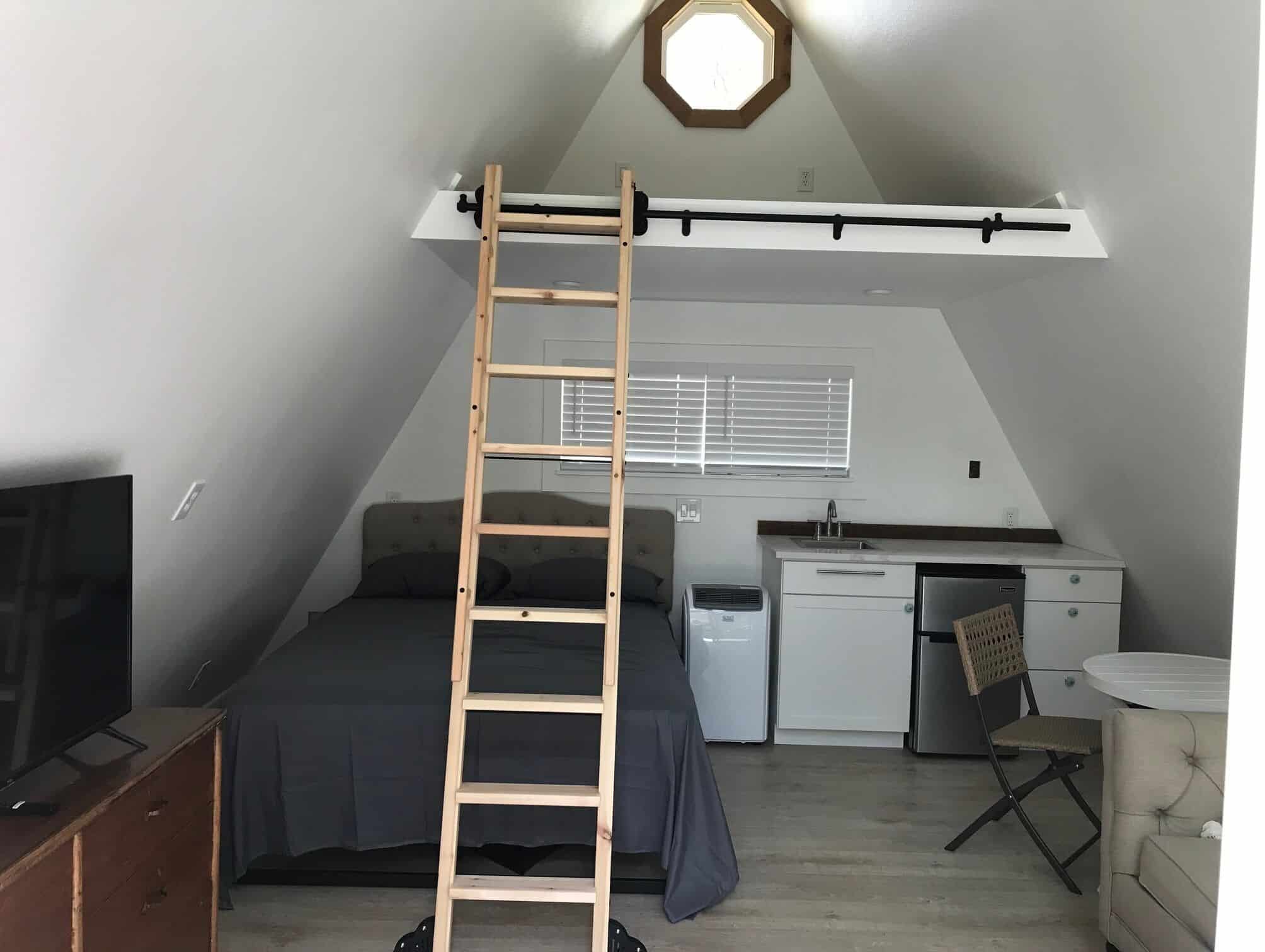 Interior of Spencer Ranch A-frame cabin with bed, ladder to loft, kitchenette, and octagon window