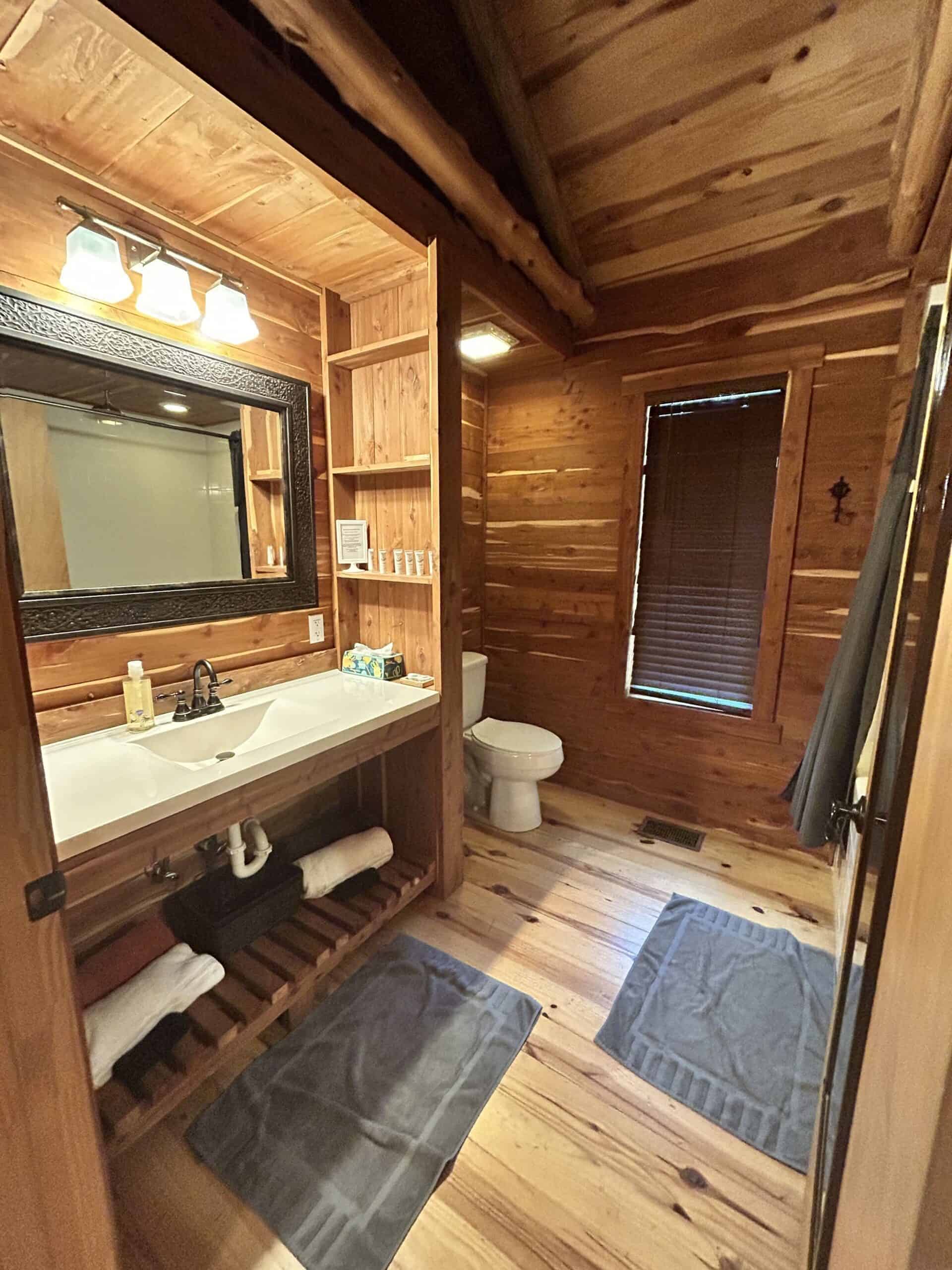 The Cabins at Angel Springs Woodland bathroom with cedar walls, vanity, and open towel shelving