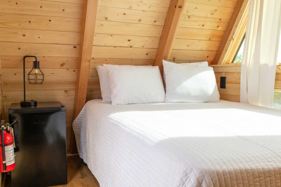 A-frame tiny house bedroom with wooden interior and large window.