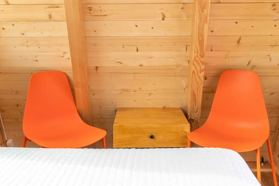 Cozy tiny house interior with wooden walls and two orange chairs beside a small wooden table.