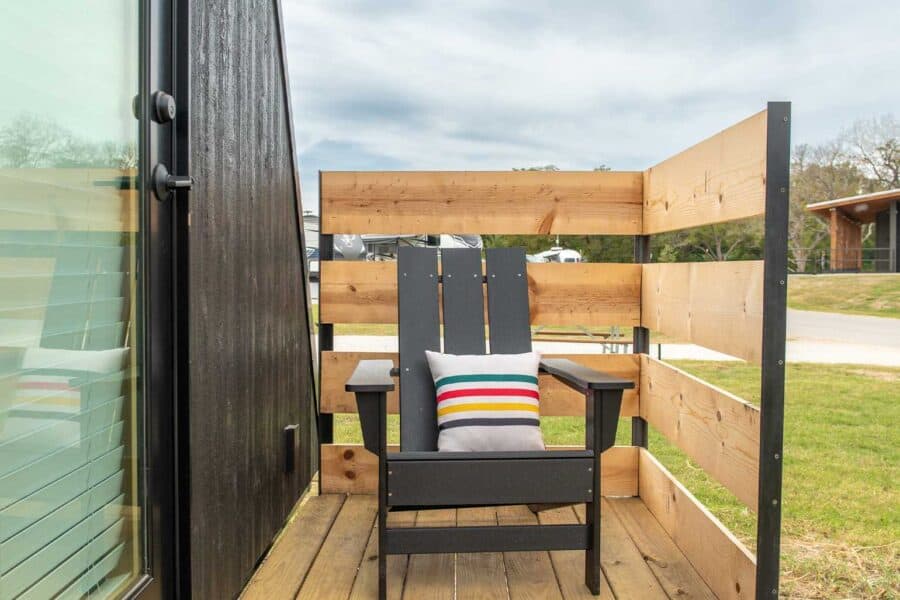 Small balcony with wooden railing and black Adirondack chair in a tiny house.