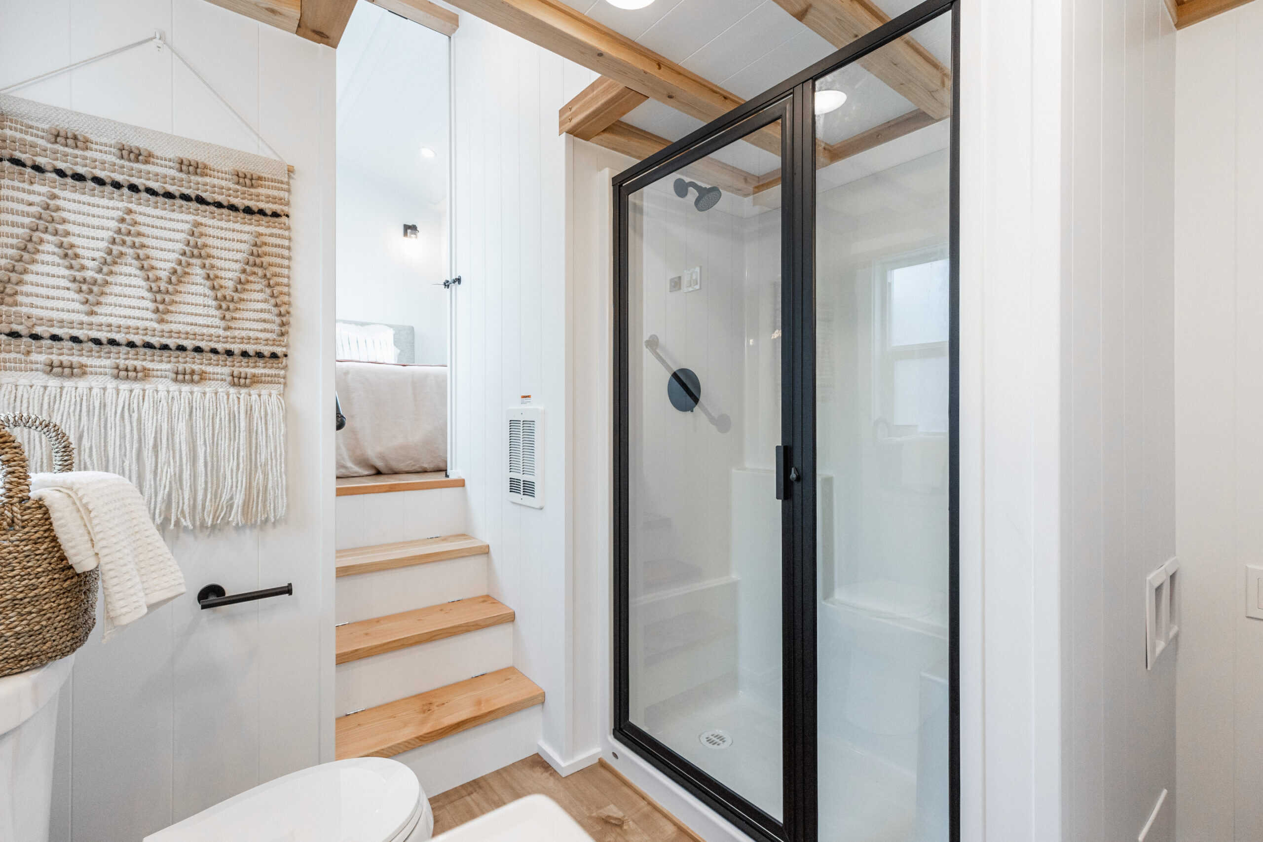 Compact tiny house bathroom with glass shower enclosure and wooden accents.