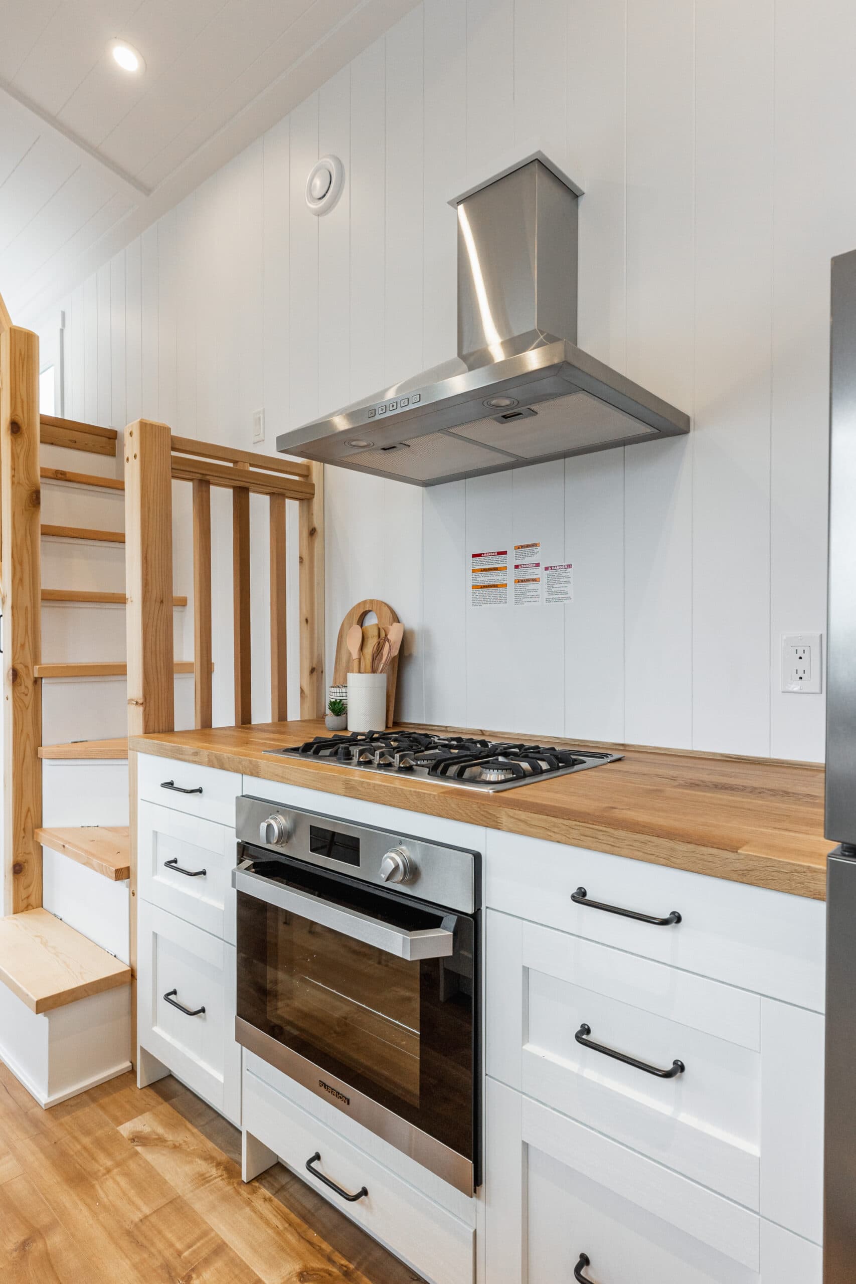 Modern tiny house kitchen with stove, oven, and stainless steel range hood.