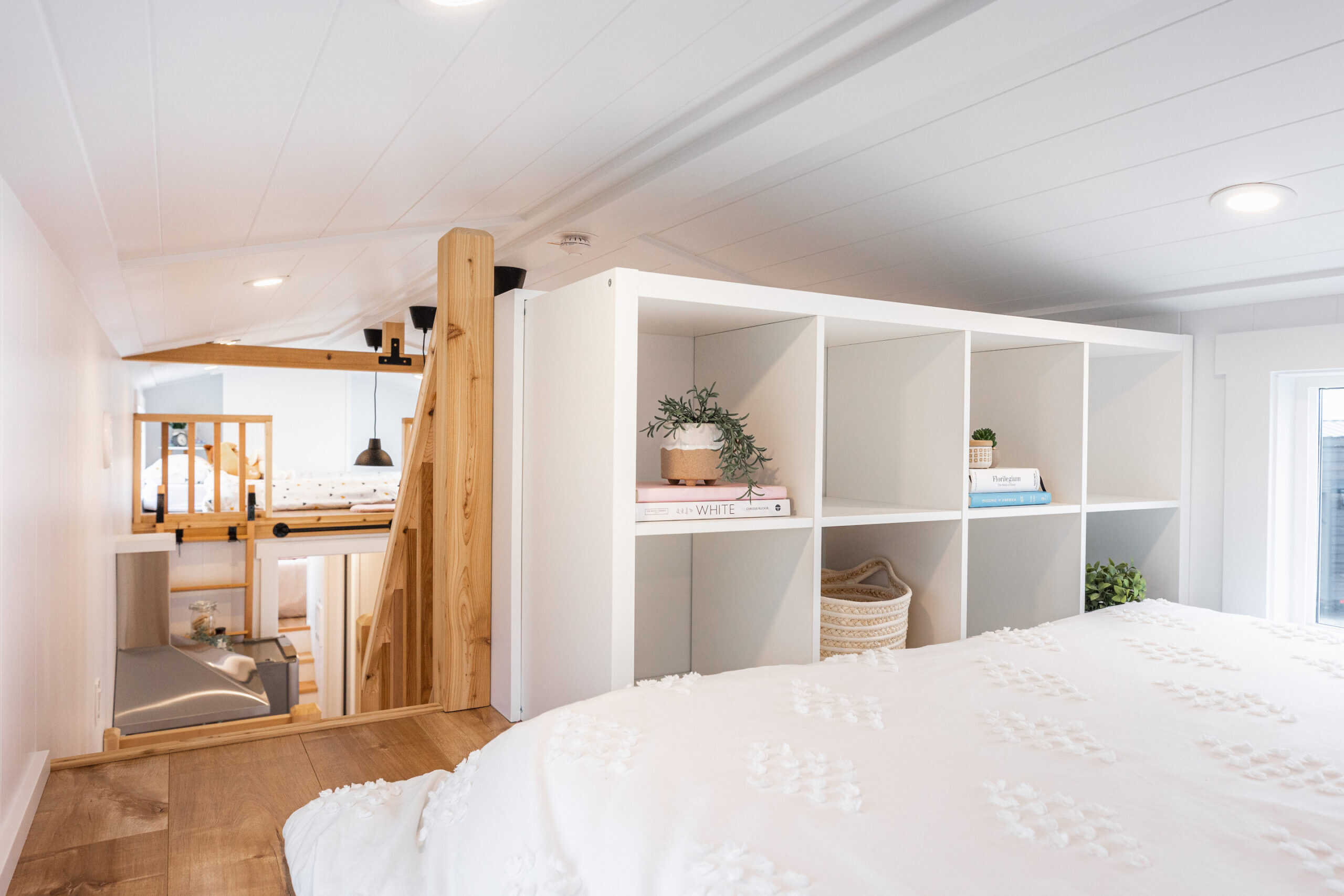 Canada Goose loft bedroom with queen bed, built-in cubby shelving as railing, and staircase down to kitchen