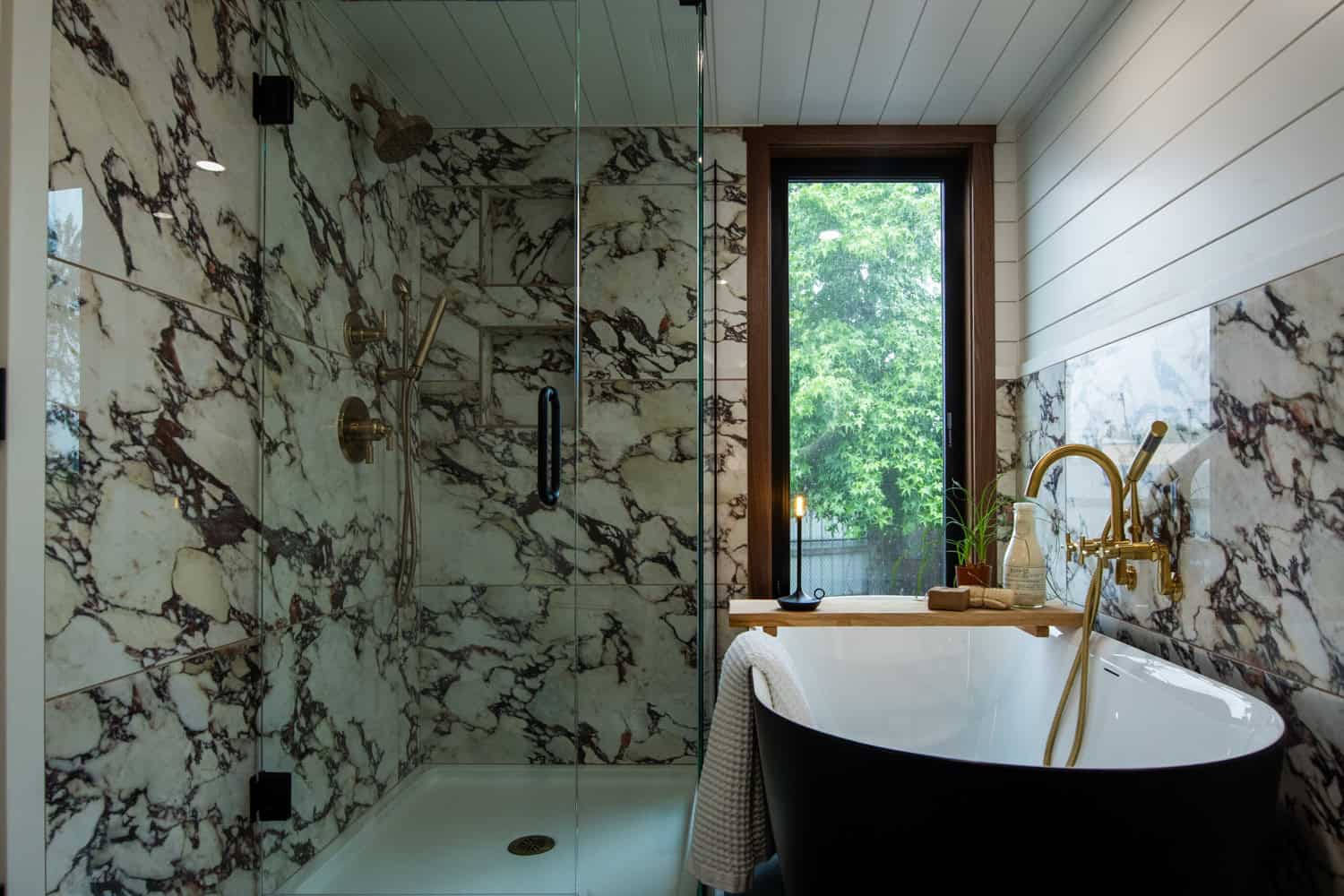 Glass-enclosed marble shower and black soaking tub with brass fixtures in the Cascade Max bathroom