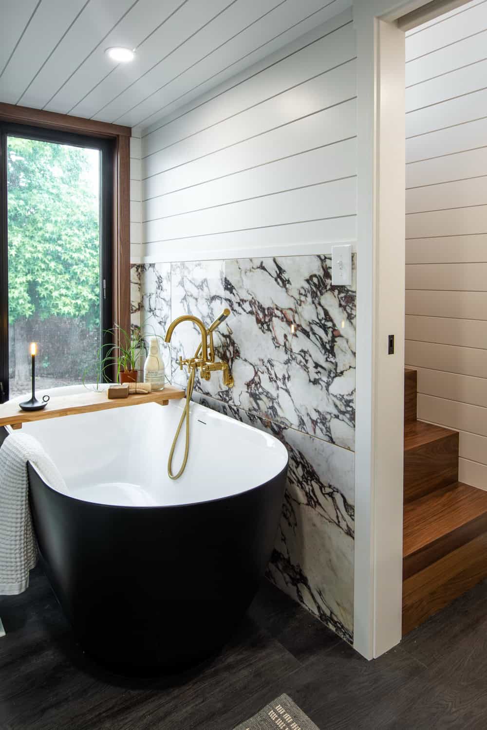 Black freestanding soaking tub against a Cala Rosso Viola marble wall with a brass tub filler in the Cascade Max bathroom