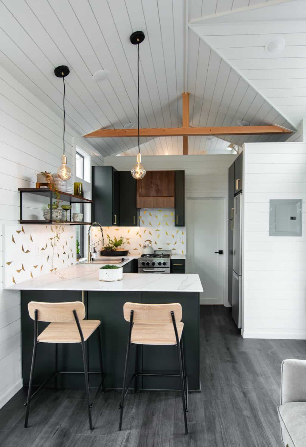 Cascade Max kitchen peninsula with two woven bar stools, dark green cabinetry, and a vaulted shiplap ceiling