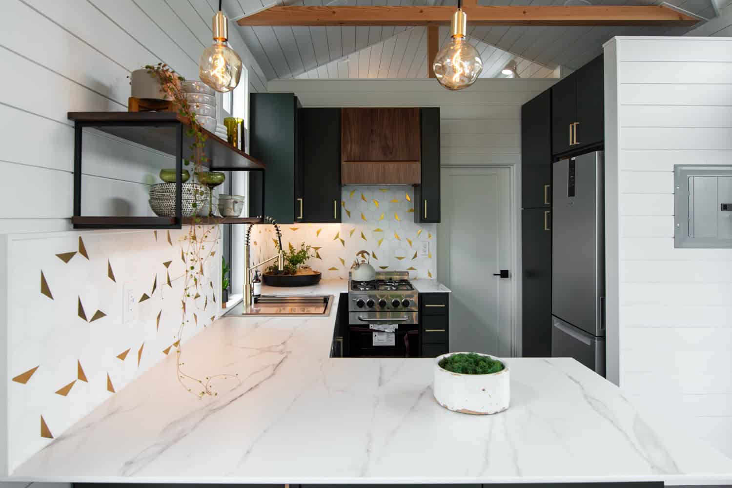 Cascade Max kitchen with marble-look counters, gold-and-white hexagon backsplash, walnut hood, and stainless refrigerator
