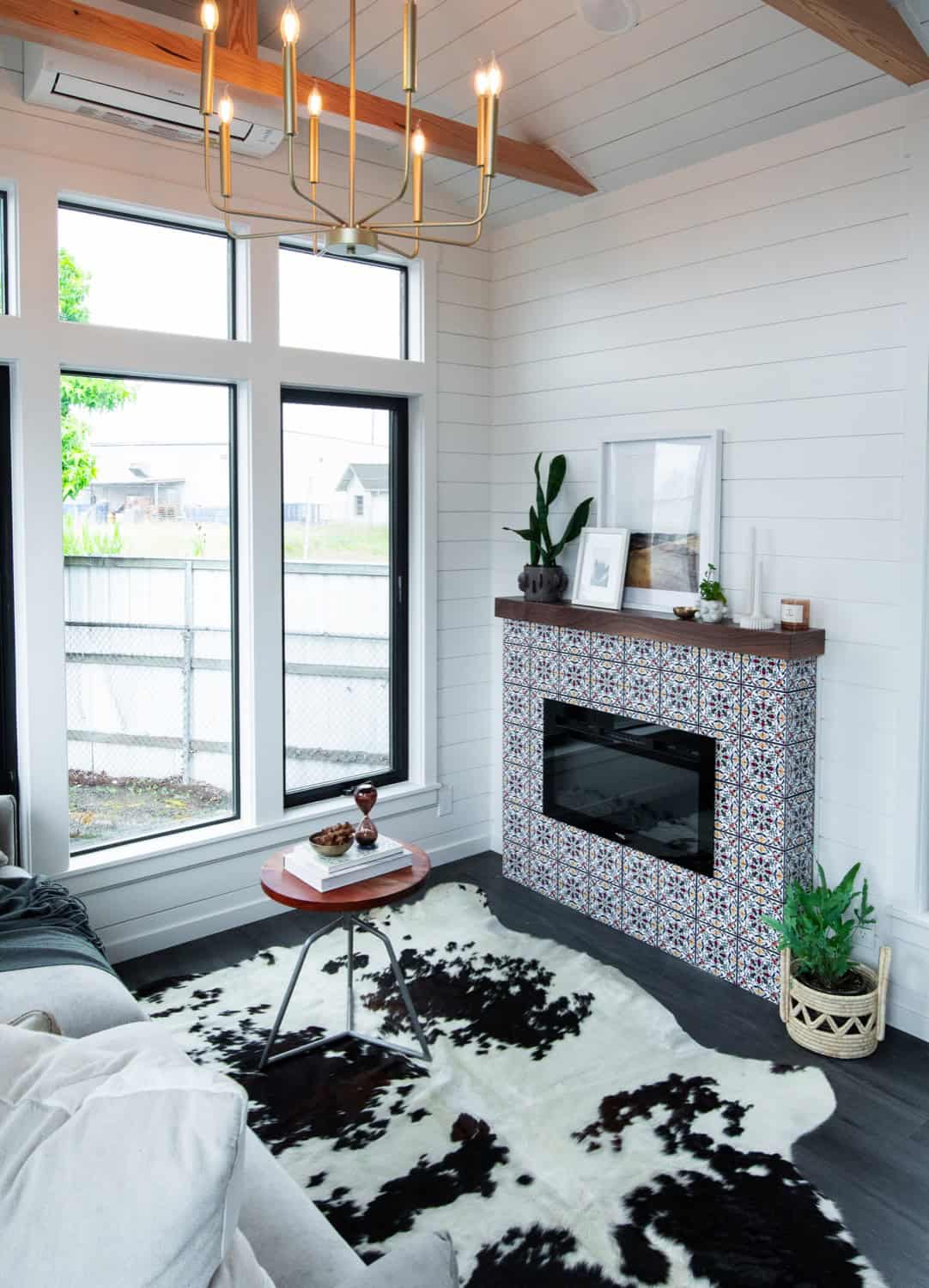 Cascade Max living room with fireplace, brass linear chandelier, and floor-to-ceiling black-framed windows