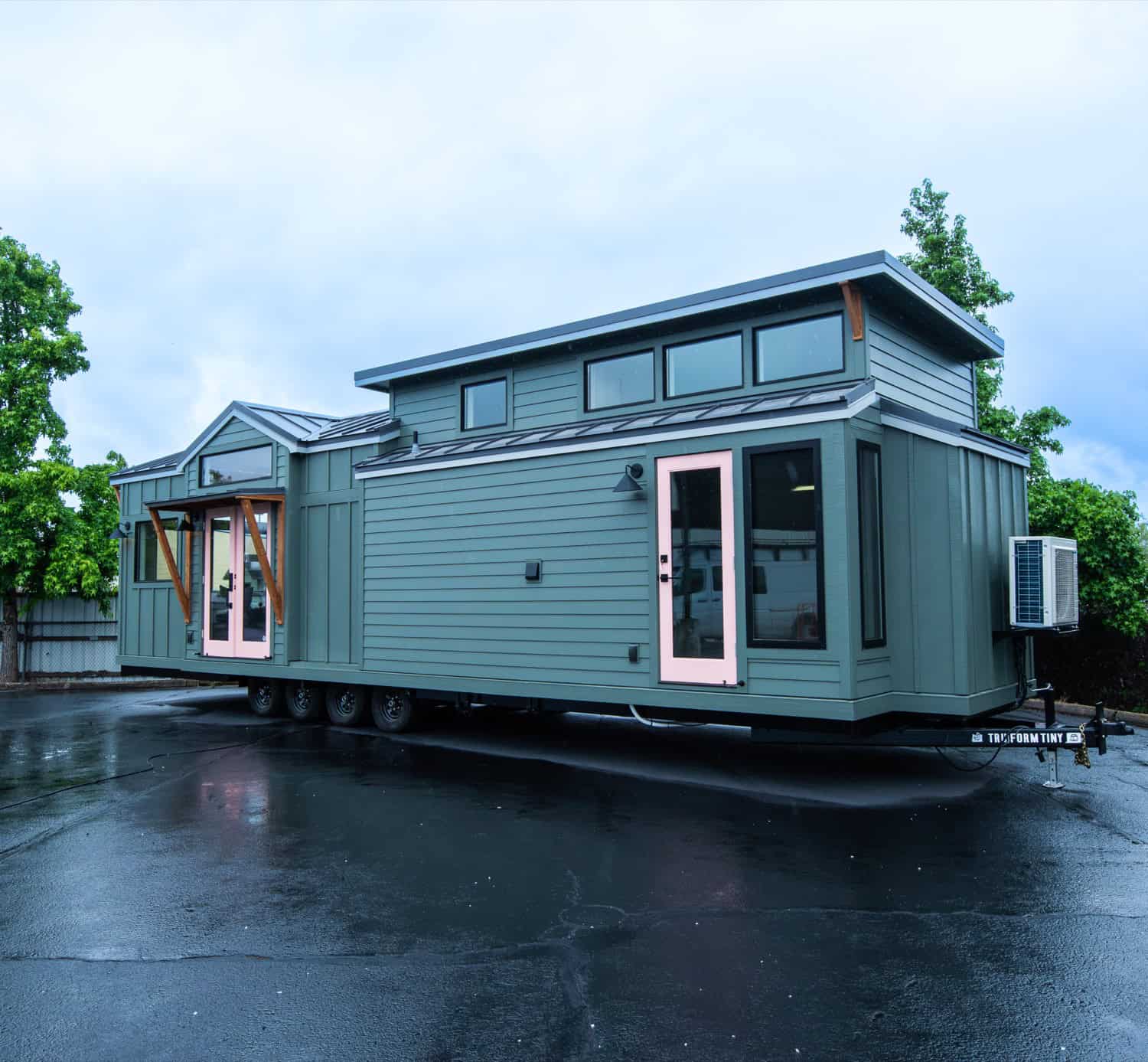 Rear three-quarter view of the Cascade Max tiny home showing the gable dormer, mini-split, and blush French doors