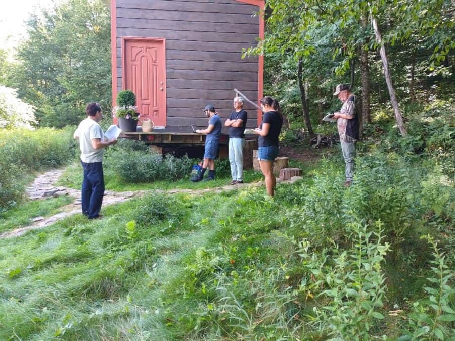 Group of people attending a tiny house workshop outdoors in a lush, green setting.