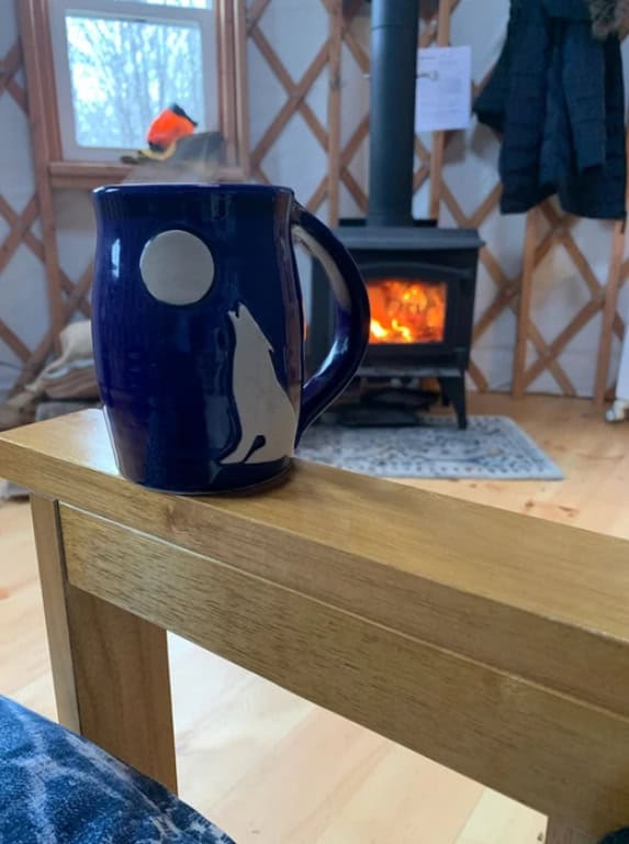 Small wooden table with blue mug inside tiny house, fireplace in background.