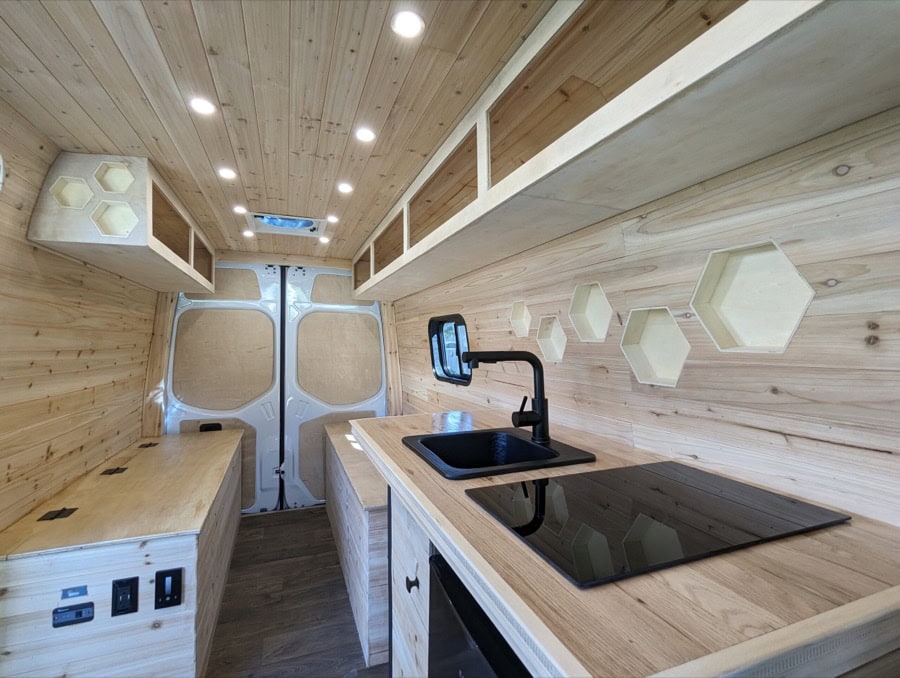 Compact cedar cabin interior with small kitchen and storage in a van conversion.