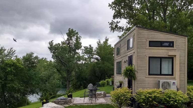 Modern tiny house with lush greenery and small outdoor seating area.