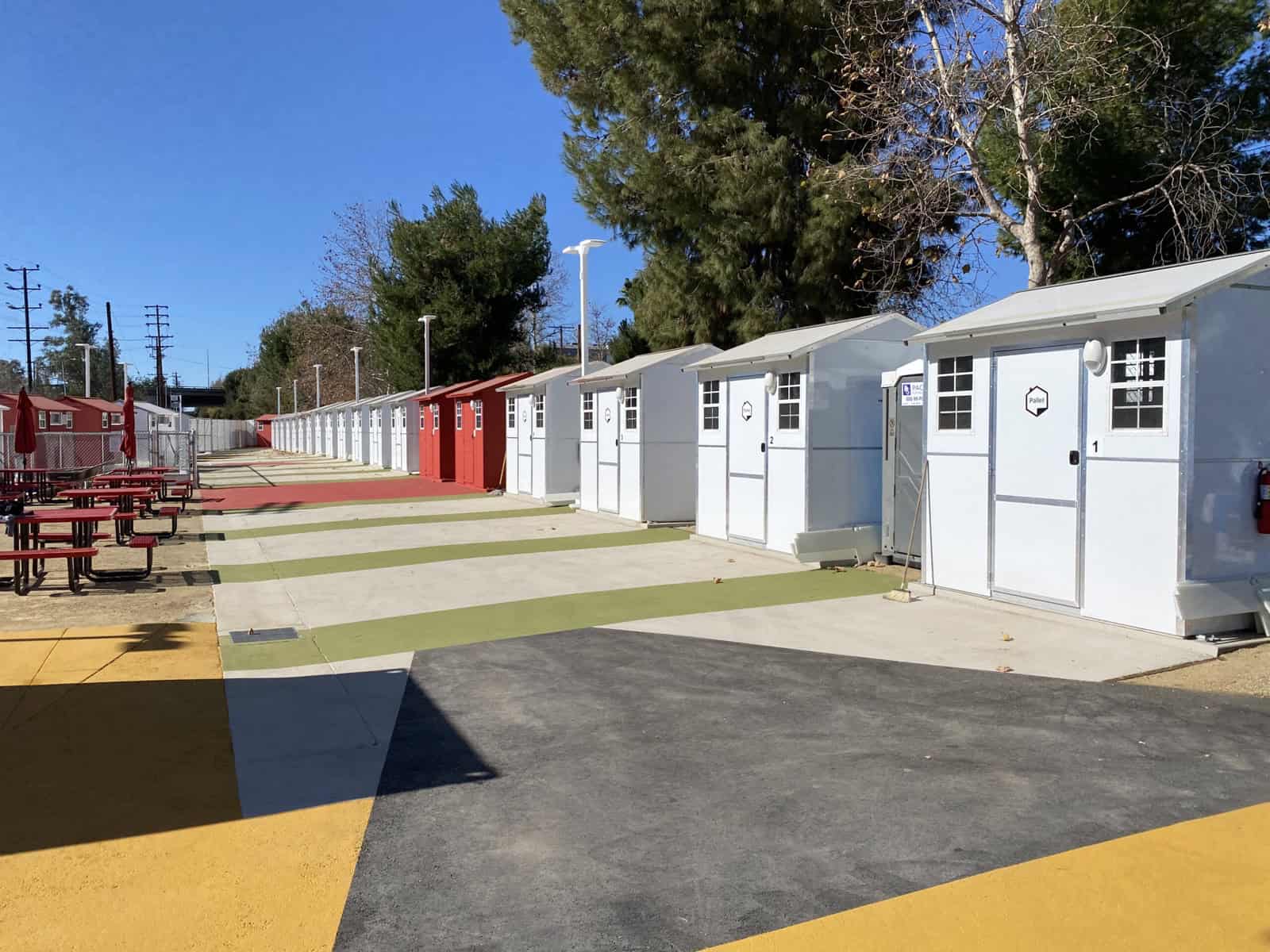 Rows of white and red Pallet tiny homes with numbered doors along colorful striped pathways at Chandler Boulevard village in North Hollywood