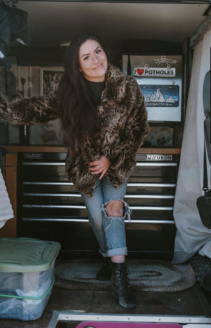 Woman in cozy fur coat inside van, embracing tiny house lifestyle.