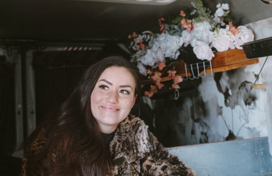 Woman enjoying her tiny van home with floral decor, embracing freedom in small spaces.