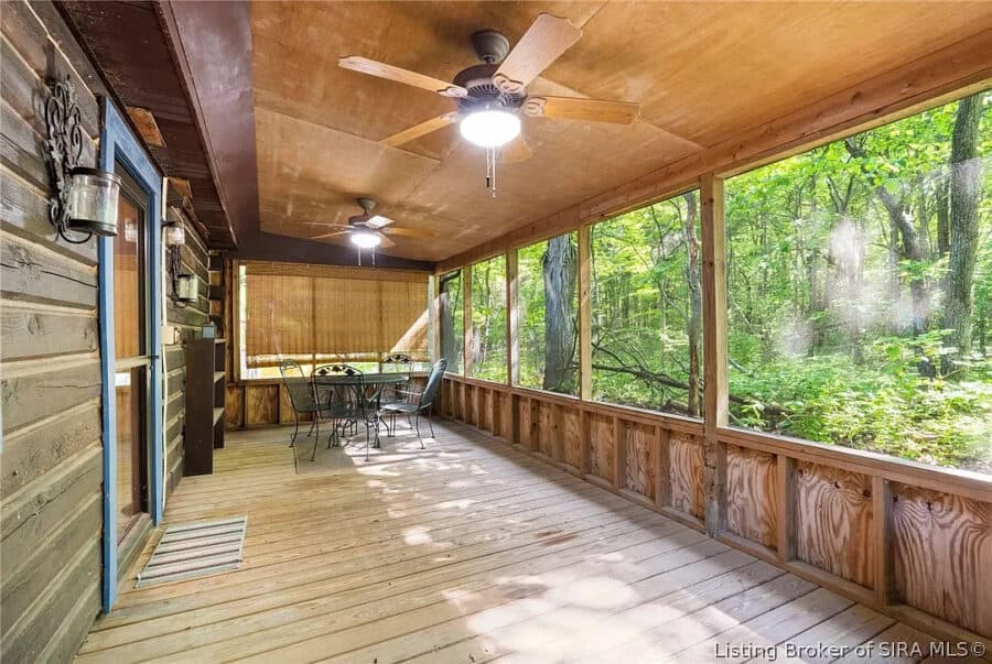 Log cabin porch overlooking lush green forest landscape.