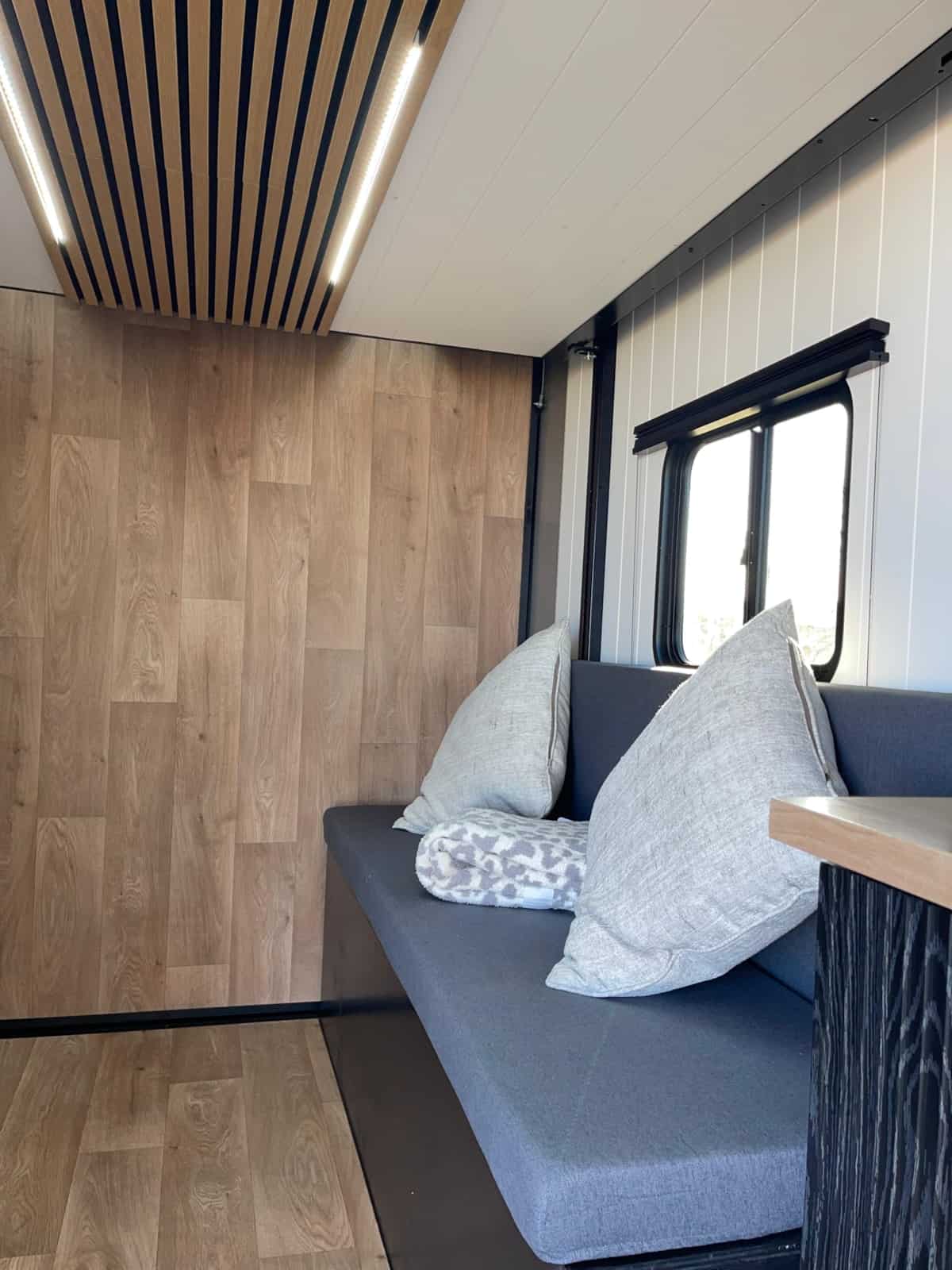Gray cushioned bench seat with pillows beneath a window inside the cargo trailer tiny home