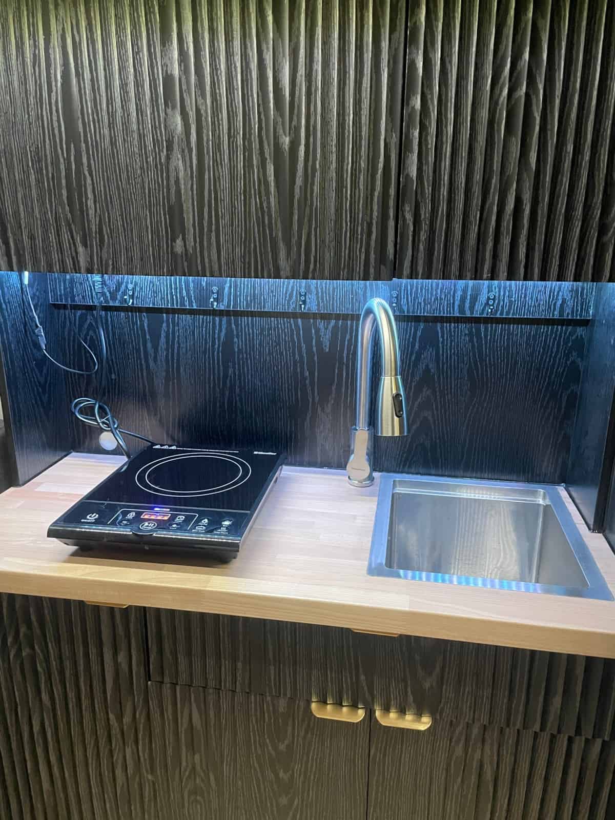 Induction cooktop and flush-mount stainless sink on a butcher block counter with black textured backsplash