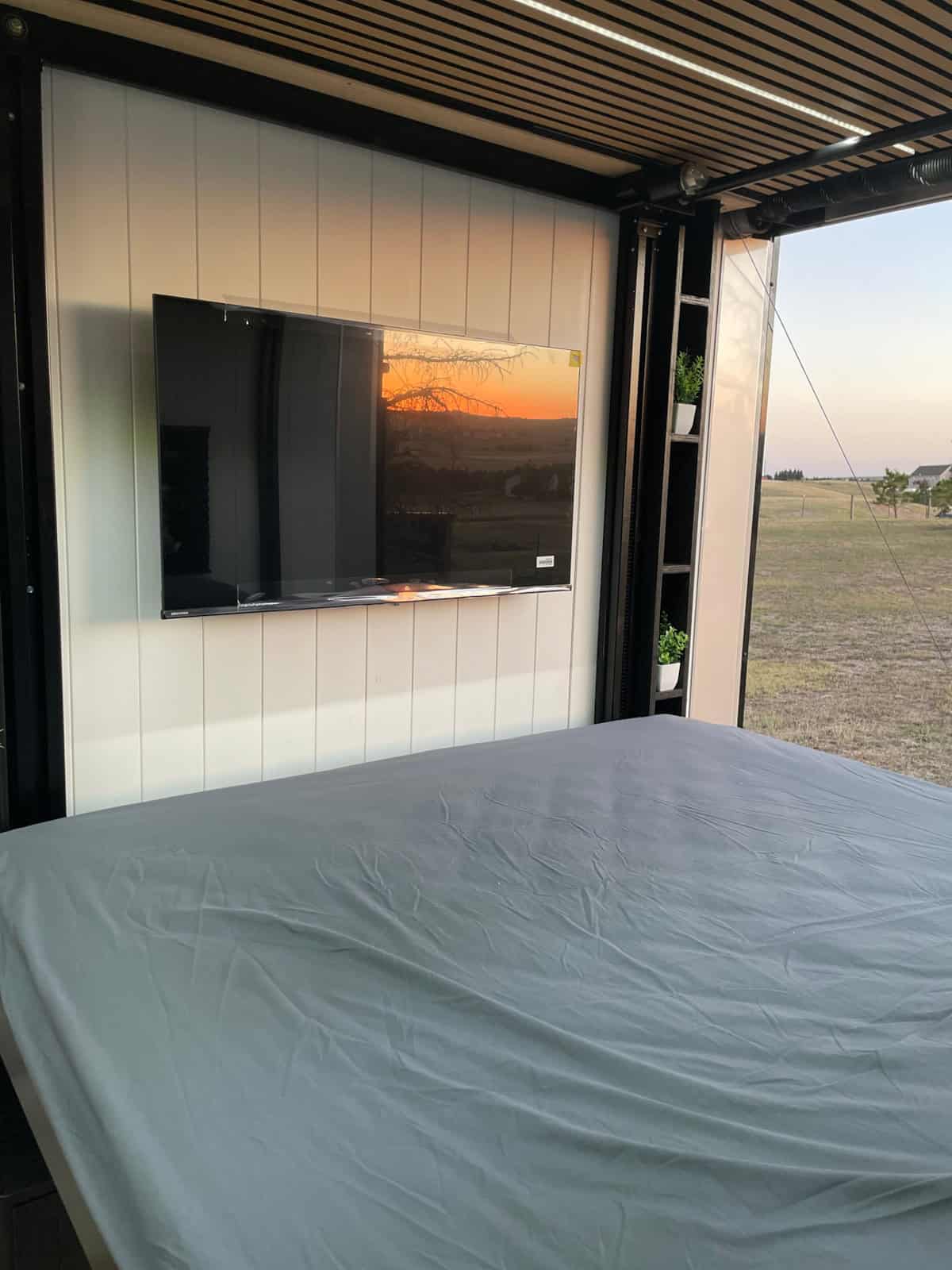 Lift bed lowered in front of the TV wall, with the side door open to a sunset view
