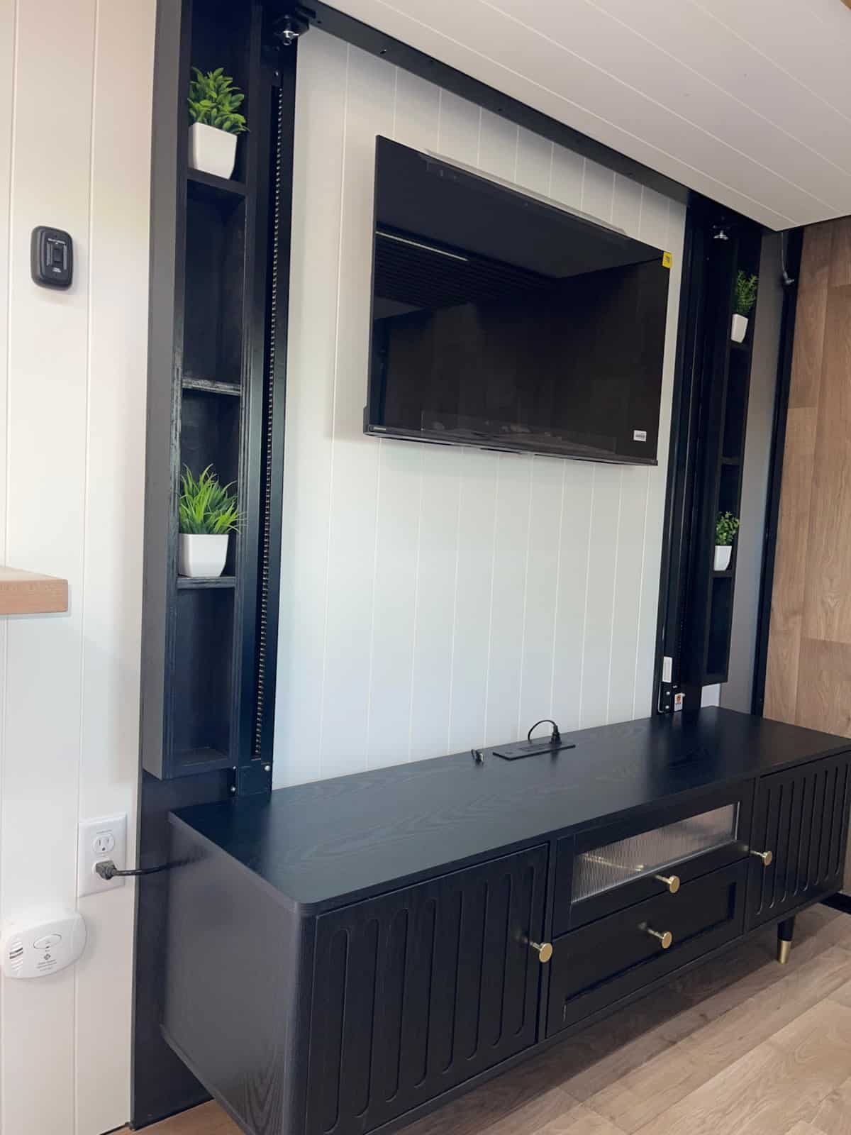 Black media cabinet with brass hardware, a wall-mounted TV, and open plant shelves