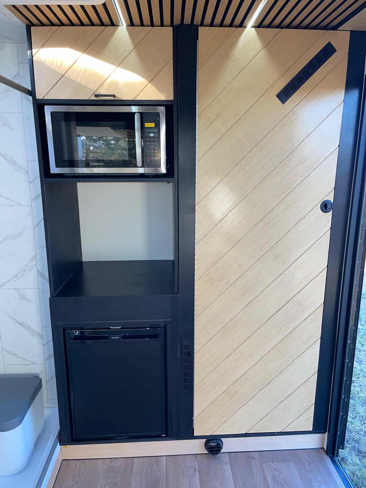 Microwave above a 12V fridge next to a wood-plank sliding bathroom door