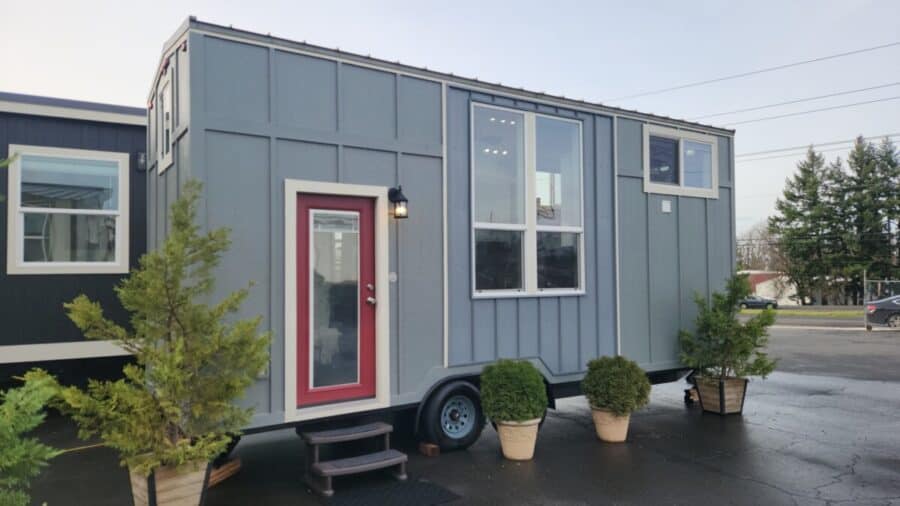 Modern tiny mountain house on wheels with large windows and red door.