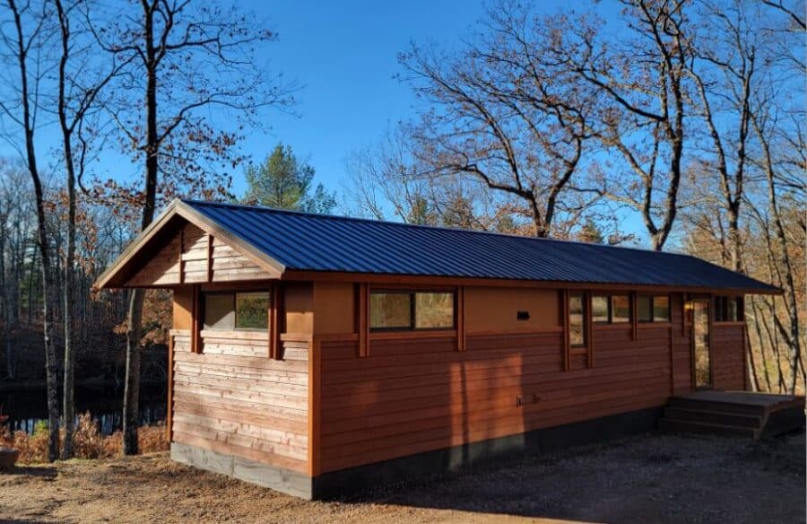 Tiny House with wooden exterior and metal roof in a wooded setting.