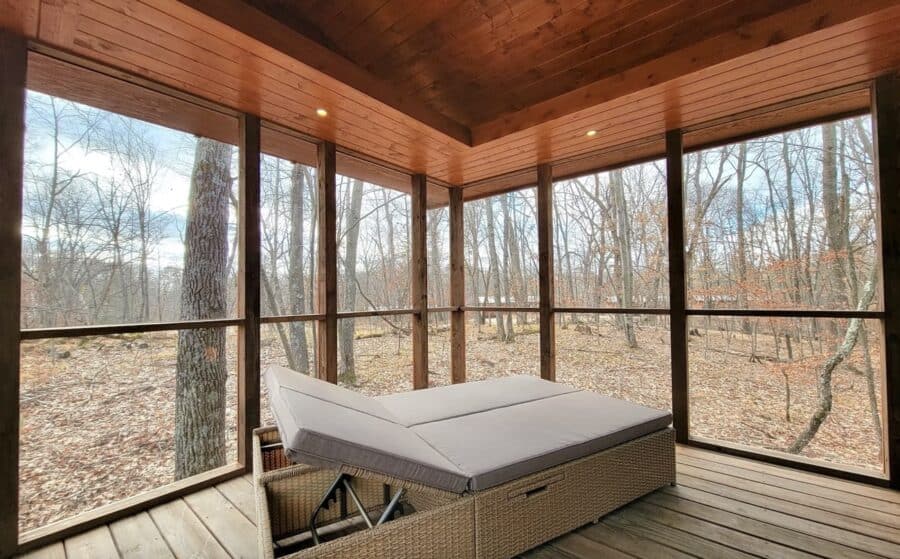 Sunlit king-sized bed in a screened porch with forest views.