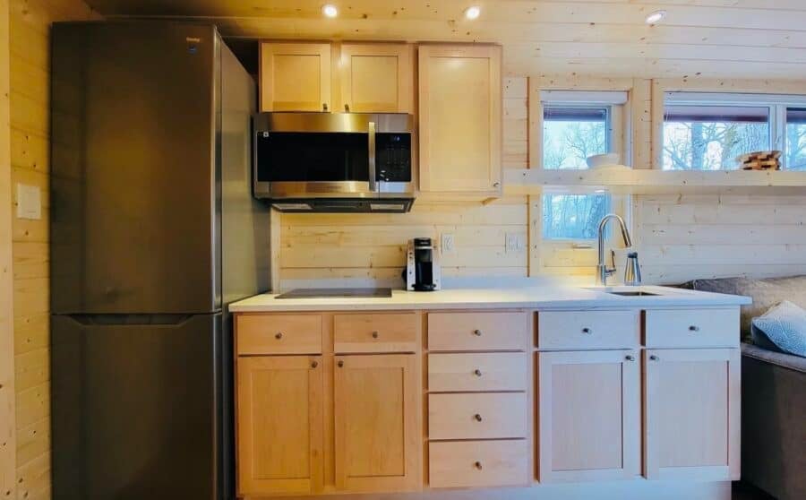 Compact kitchen with light wood cabinets and modern appliances in a luxury tiny home.