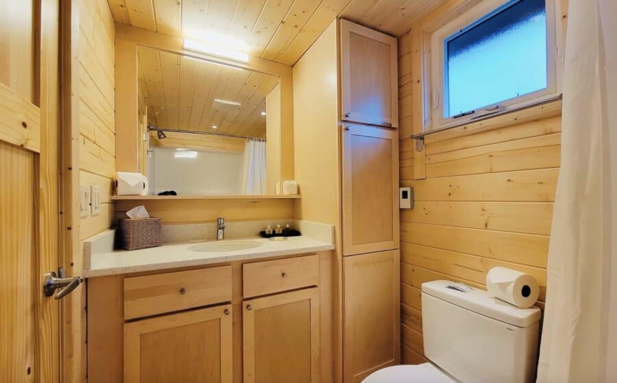 Cozy wooden tiny house bathroom with sink, mirror, and toilet in a compact space.