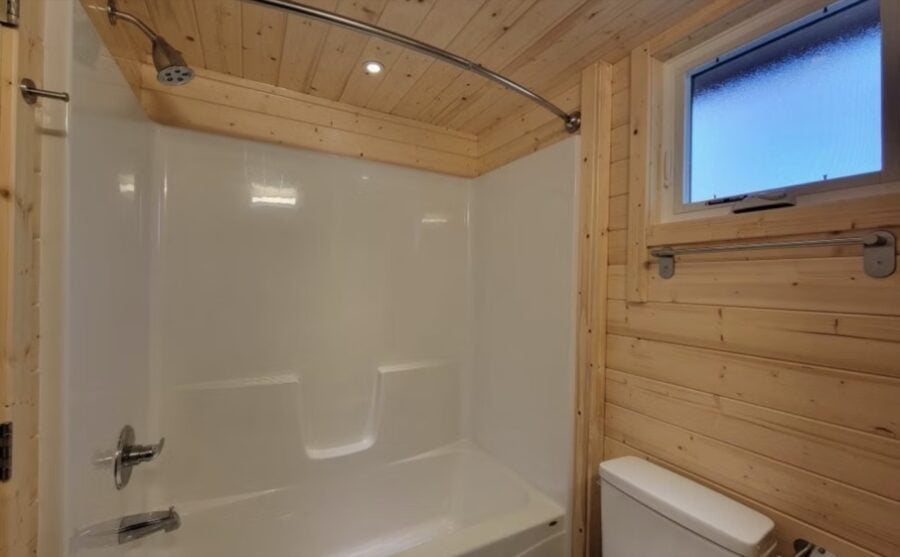 Cozy wooden tiny house bathroom with shower and small window.