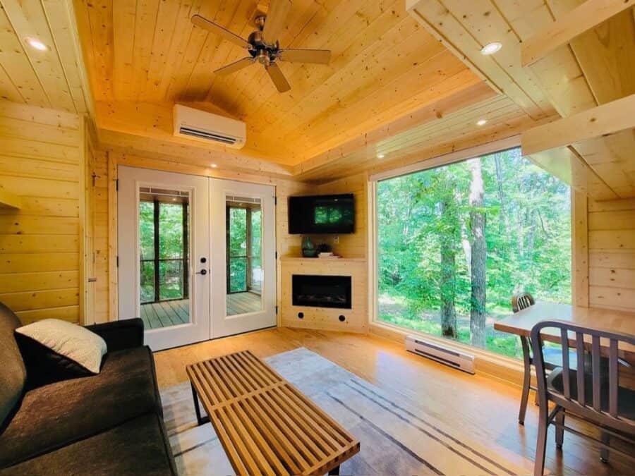 Tiny house interior with large windows overlooking lush forest scenery.