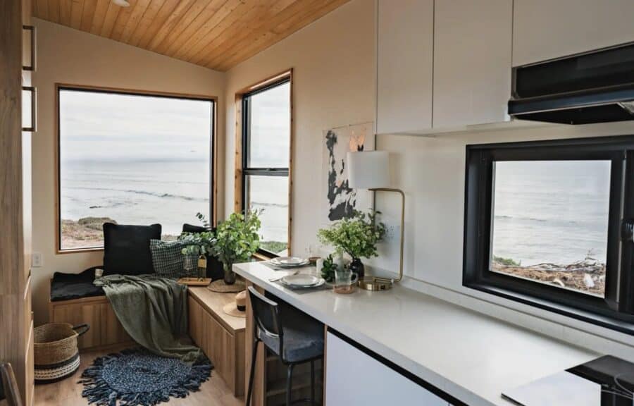 Cozy tiny house with large windows showcasing ocean views and modern decor.