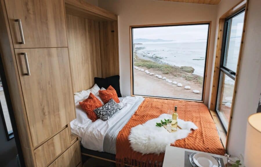 Cozy tiny house bedroom with large window overlooking the ocean.