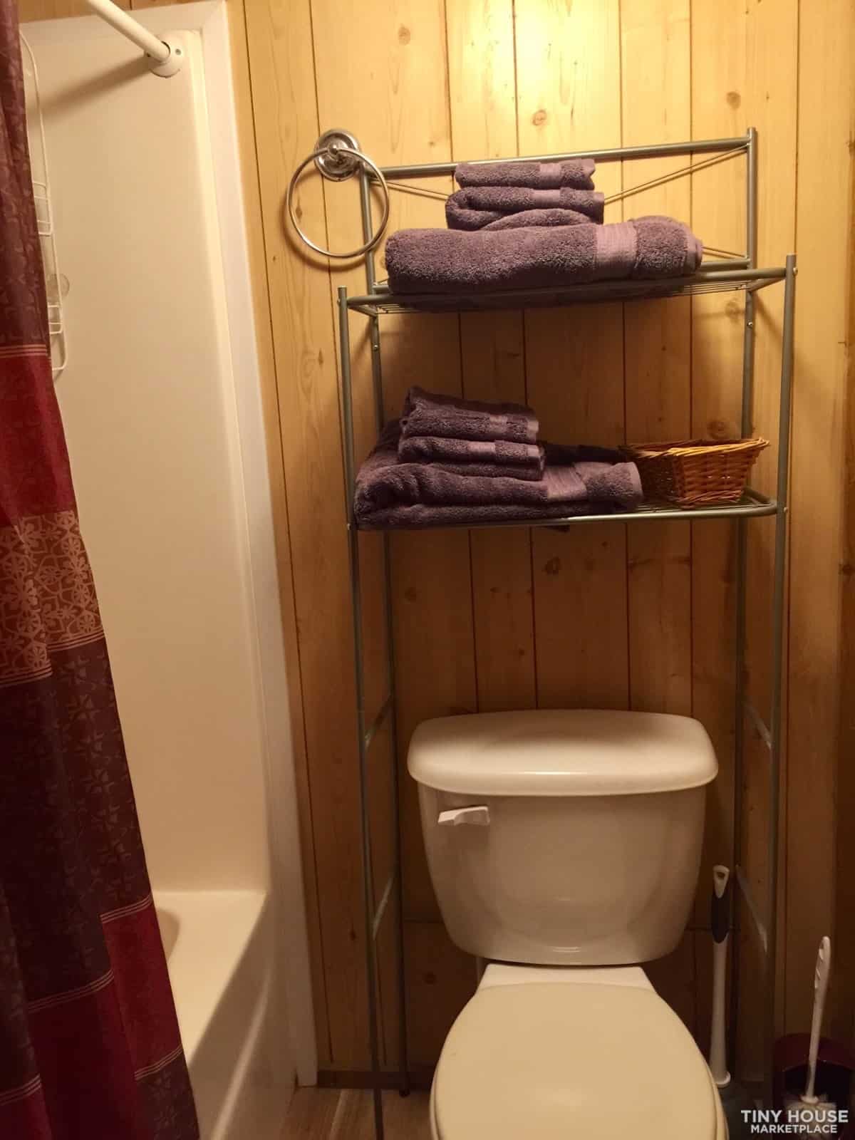 Full tub and shower combination with a shower curtain and over-toilet storage shelving in the bathroom.