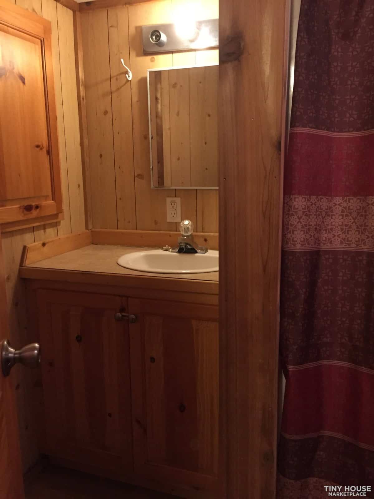 Bathroom vanity with pine cabinetry, mirror, and shelf in the Country Cottage tiny home.