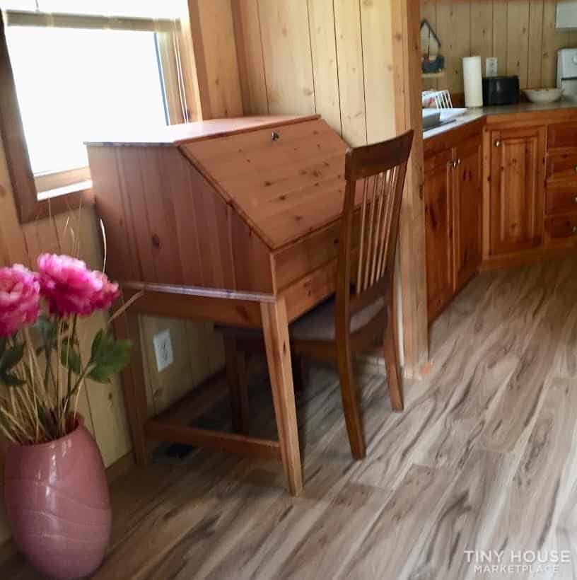 Drop-front wooden writing desk and chair set beside a window in the pine-lined interior.