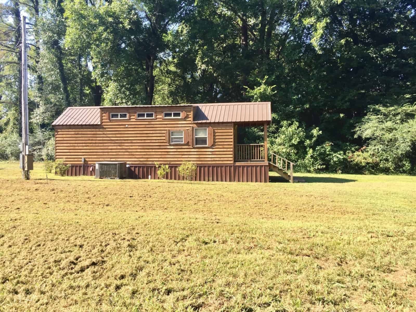 Country Cottage park model tiny home with cedar lap siding and a metal roof sitting in an open field on three acres in Williston, Tennessee.