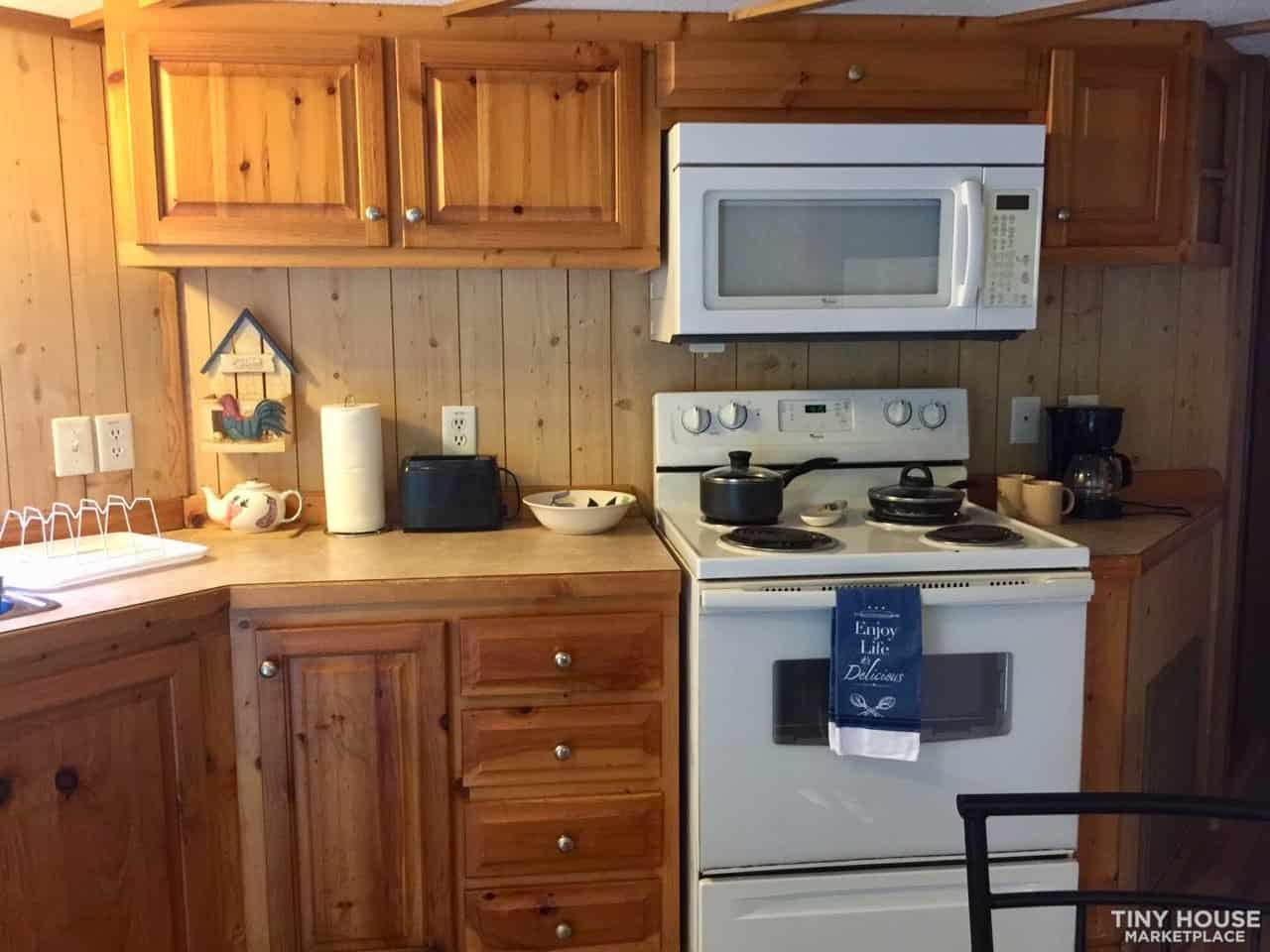 Close view of the pine kitchen cabinetry, electric range, and countertop workspace in the park model tiny home.